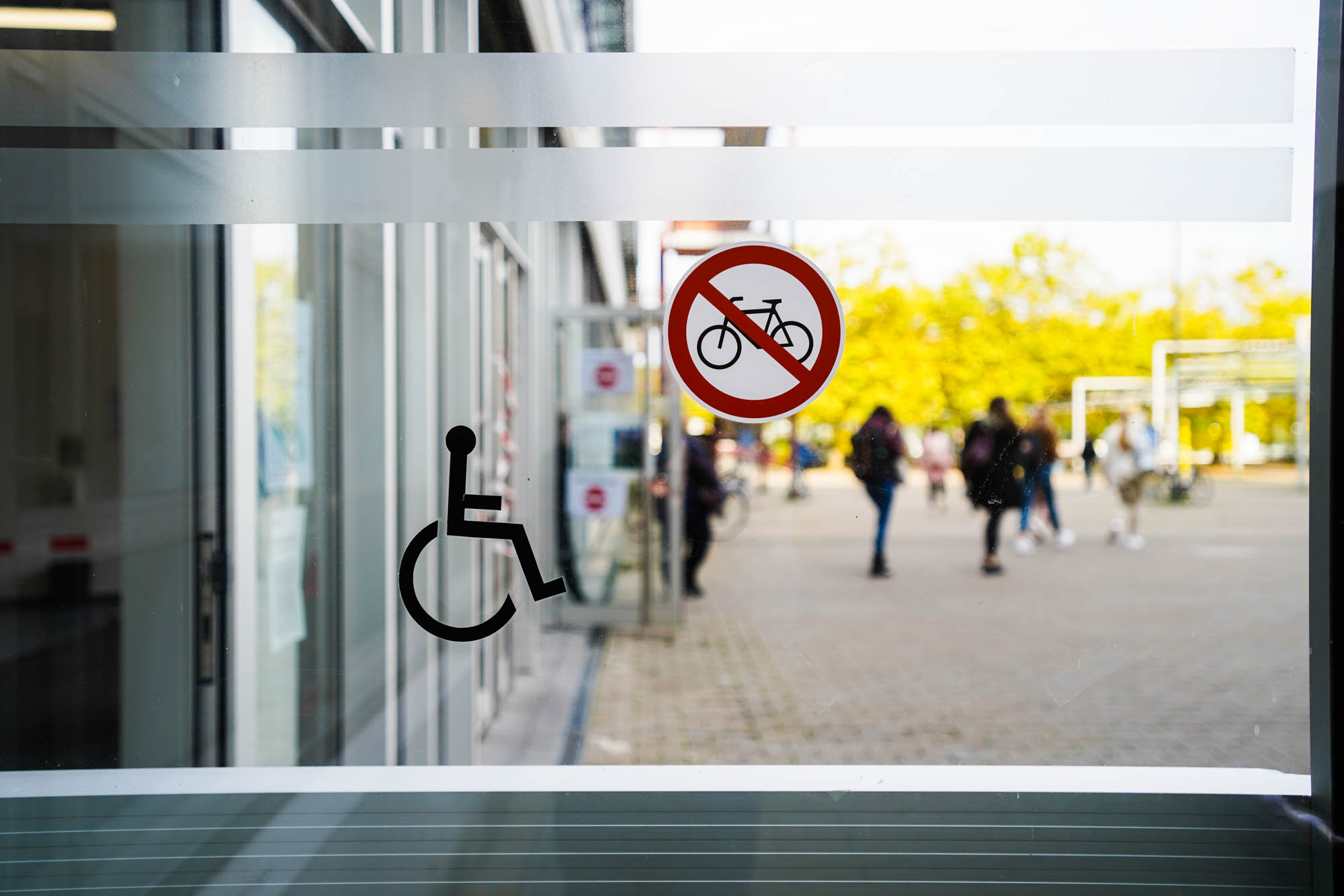 Eingangstür zur Uni Bielefeld mit Symbol eines Rollstuhlfahrers und einem Fahrrad-Verbotsschild