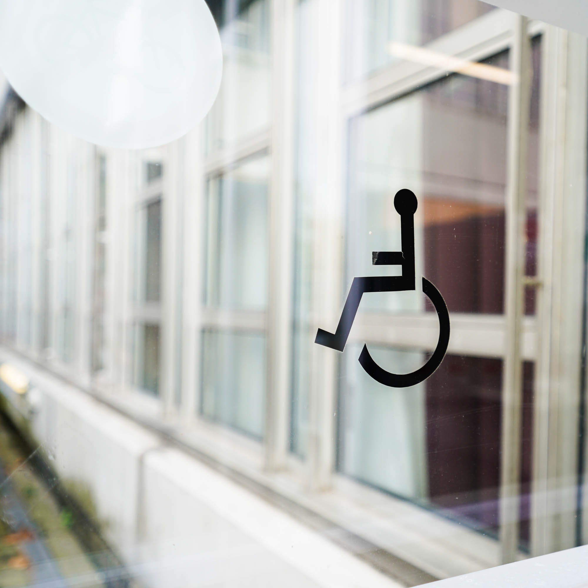 Auf einer Glastüre das abstrakte Zeichen eines Rollstuhlfahrers