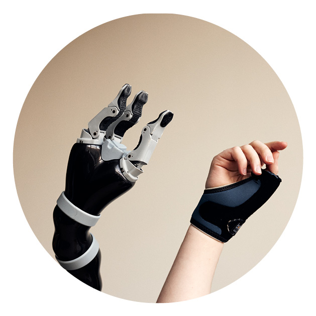 Eine Roboterhand wird neben einer menschlichen Hand vor einem sandfarbenen Hintergrund in die Luft gestreckt